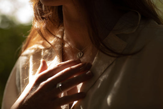 Person wearing a necklace with a textured pendant in a softly lit setting