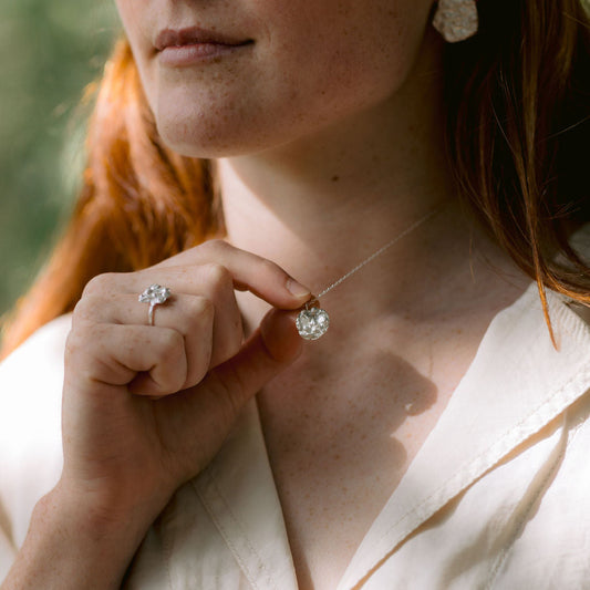 Close-up of a person wearing a necklace and ring with a blurred background