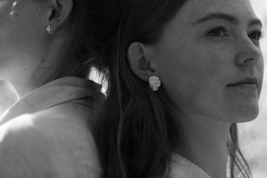 Close-up of a woman wearing diamond earrings with another person partially visible.