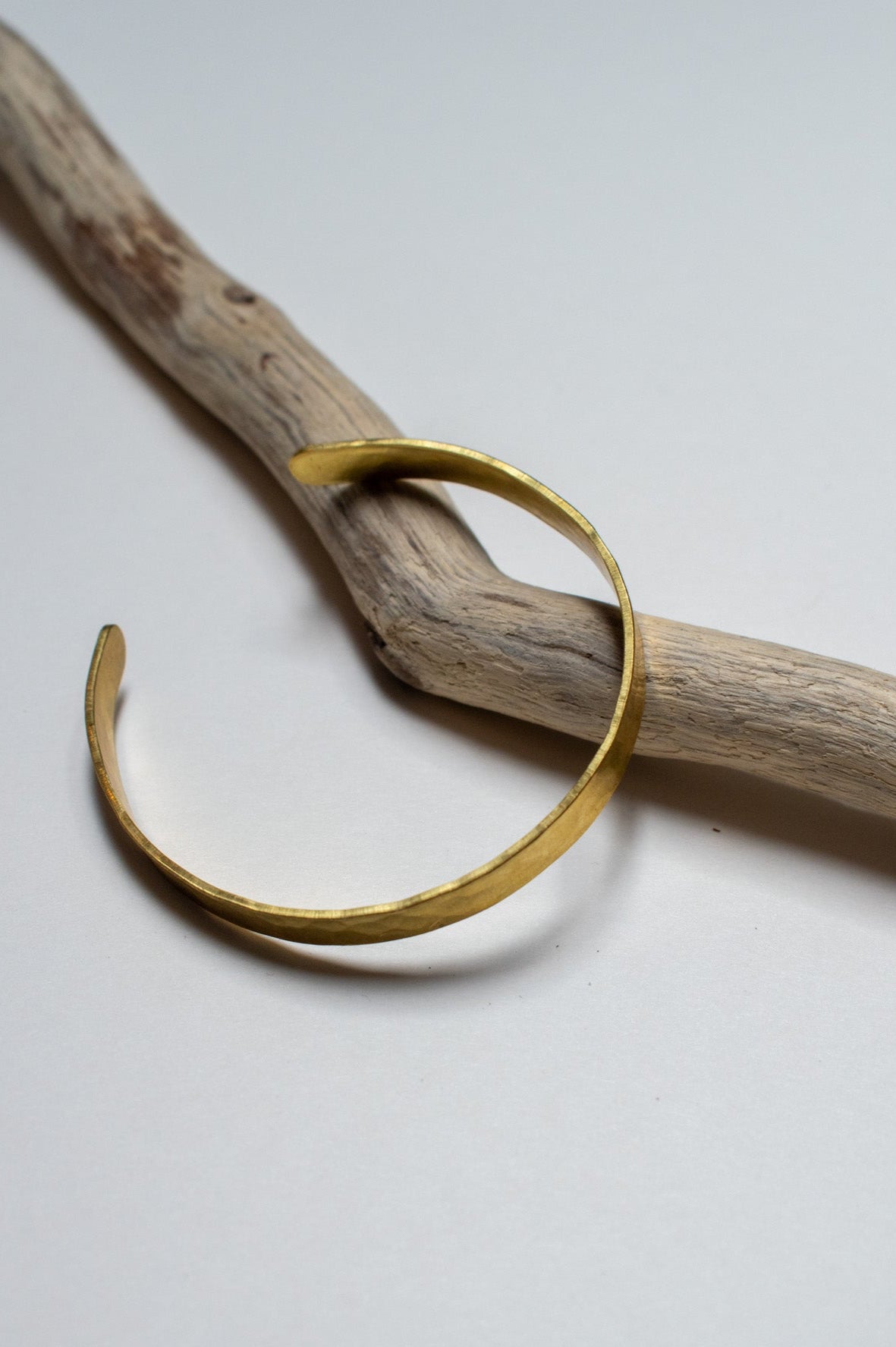 brass bracelet on a piece of driftwood against a white background
