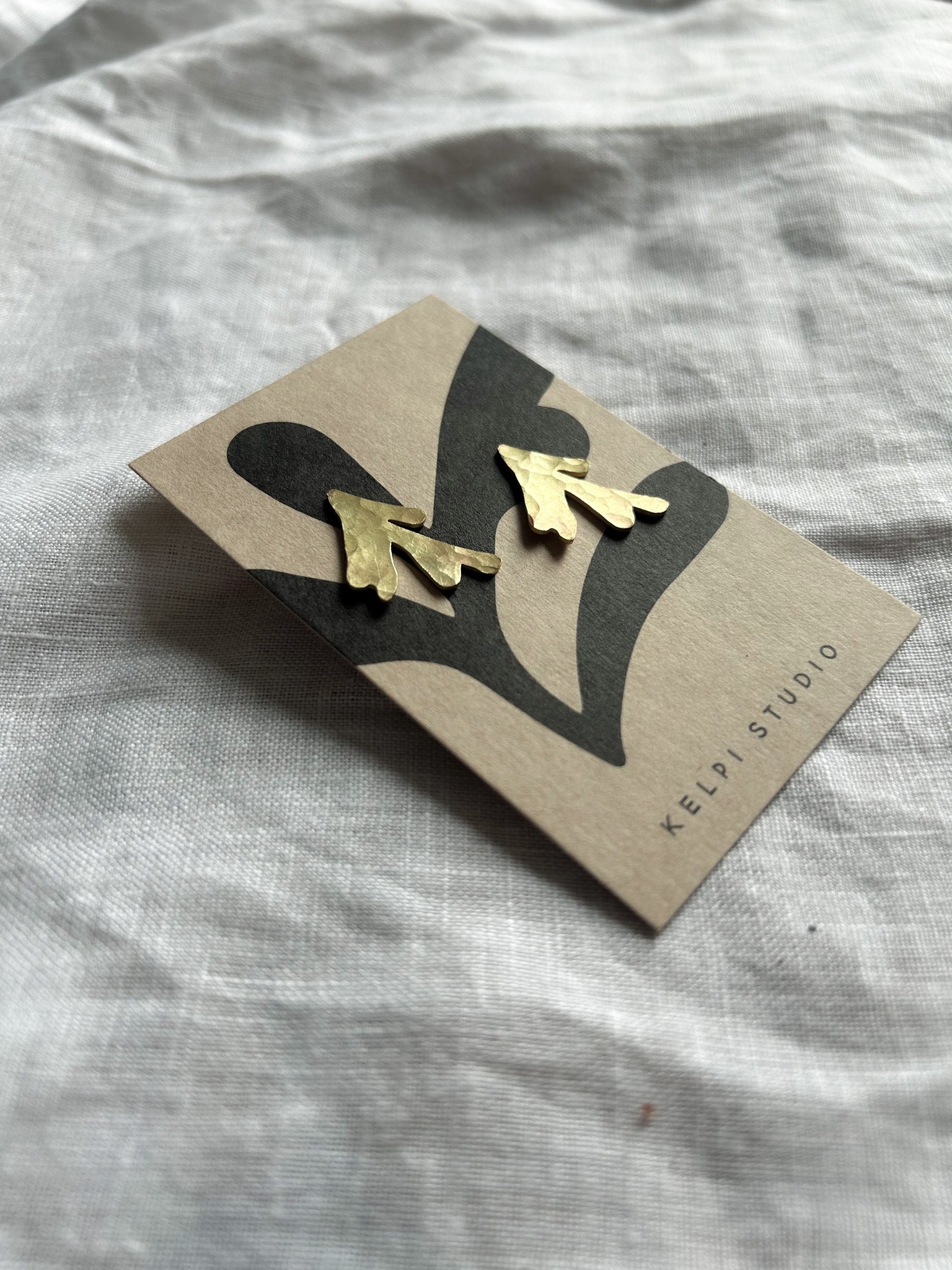 brass seaweed earrings on a Kelpi Studio branded card against a light  fabric background