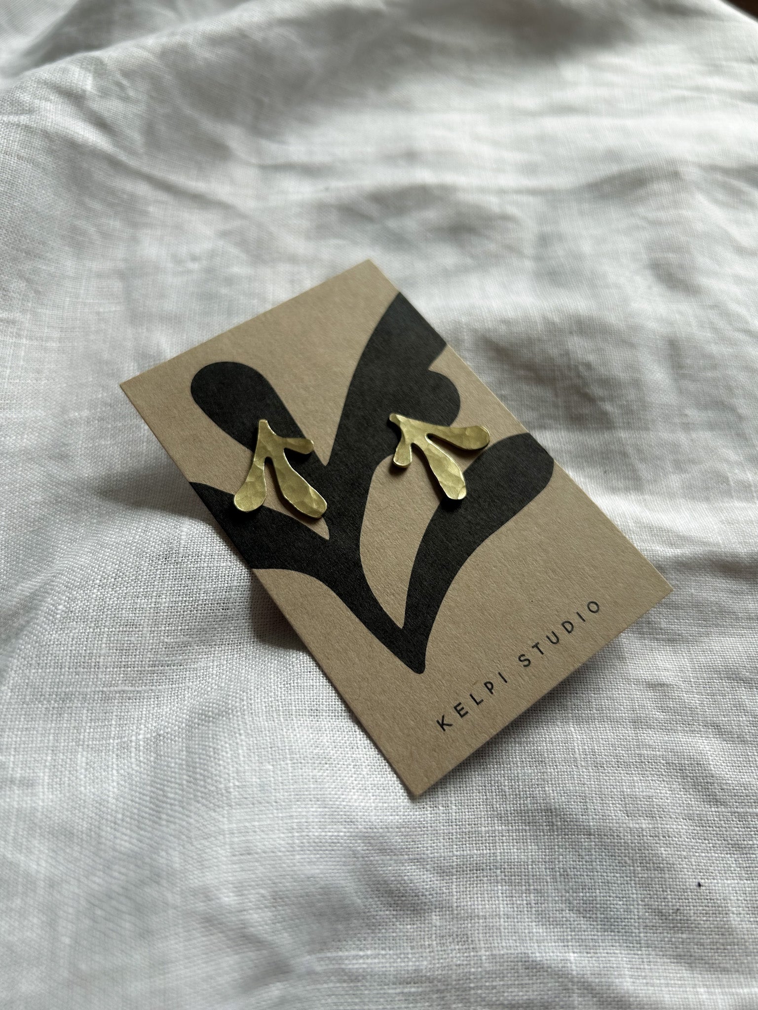 Brass earrings on a Kelpi card on a light  fabric background