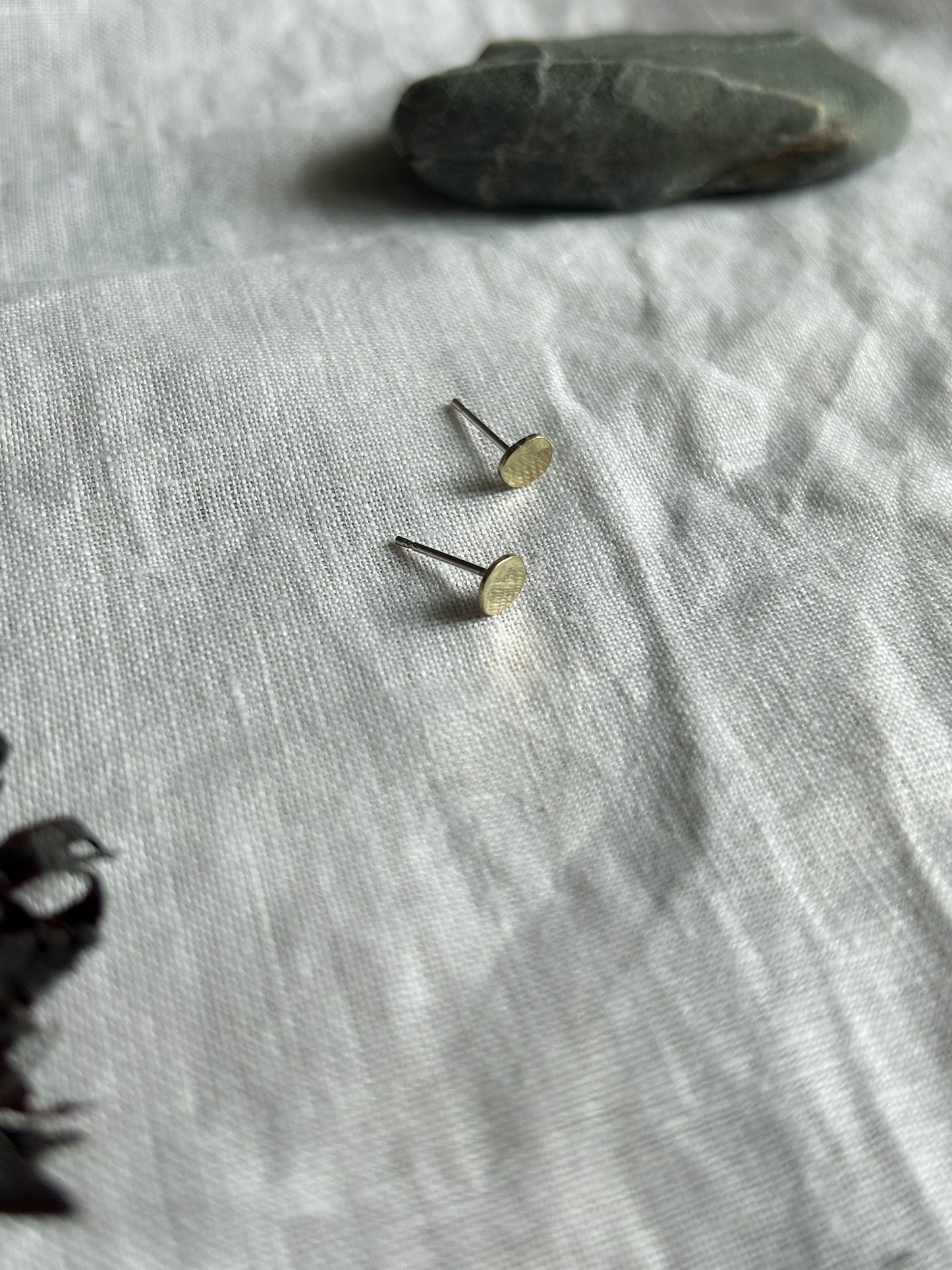 Small gold earrings on a textured gray fabric surface