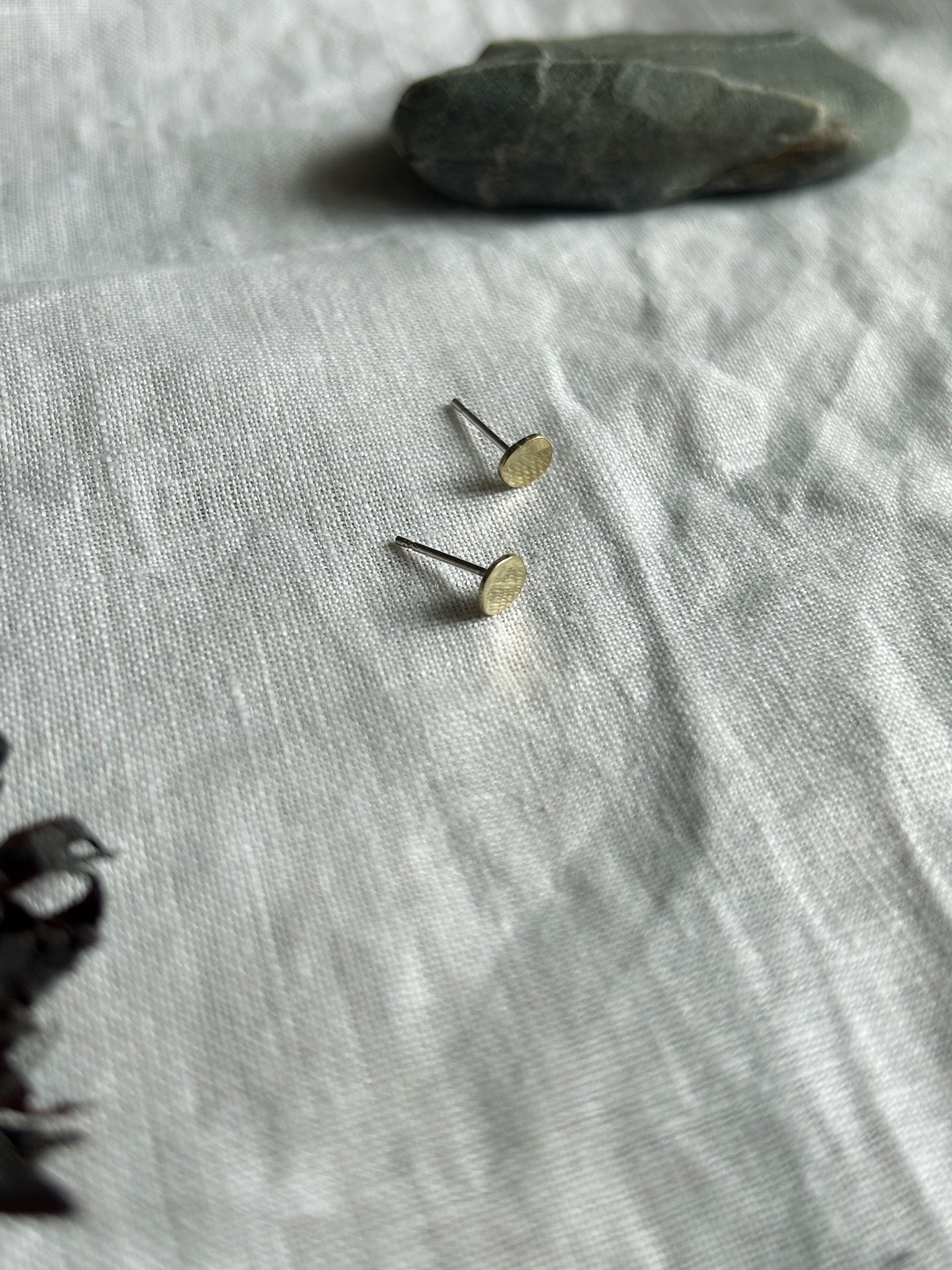 Small gold earrings on a textured gray fabric surface