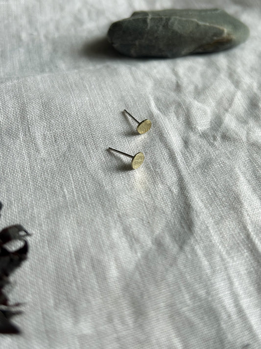 Small gold earrings on a textured gray fabric surface