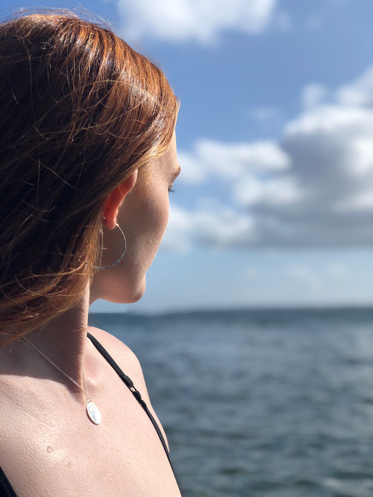 Woman looking at the sea with a necklace with a silver pendant.