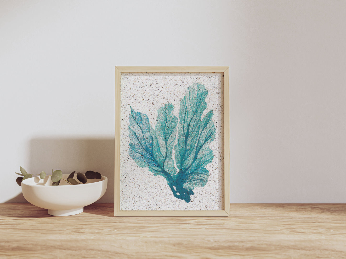 Framed artwork of teal coral placed on a wooden surface with a neutral background.