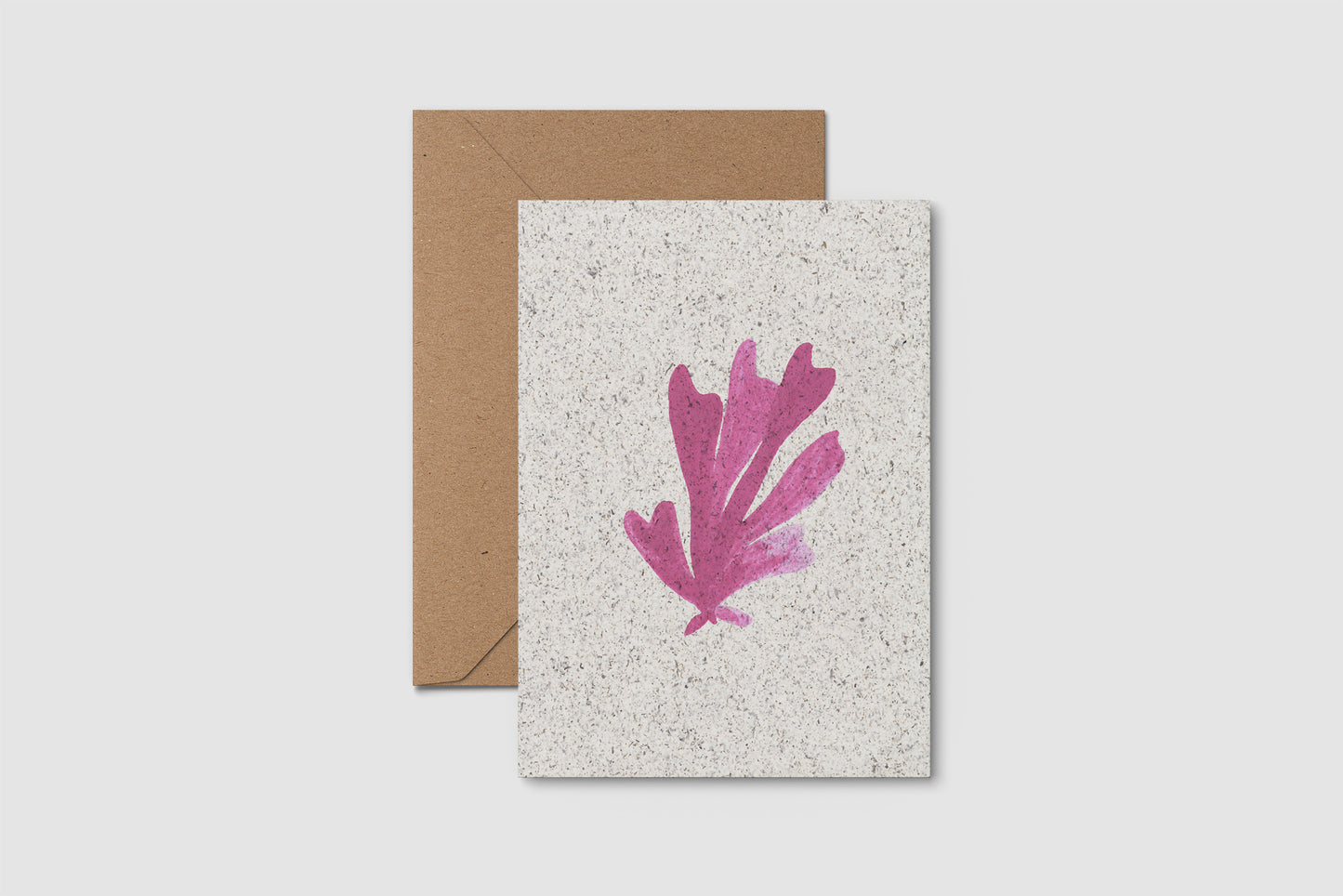 Card with pink leaf design and brown envelope on a light gray background
