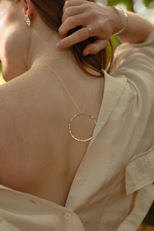 Person wearing a necklace with a circular pendant, back view