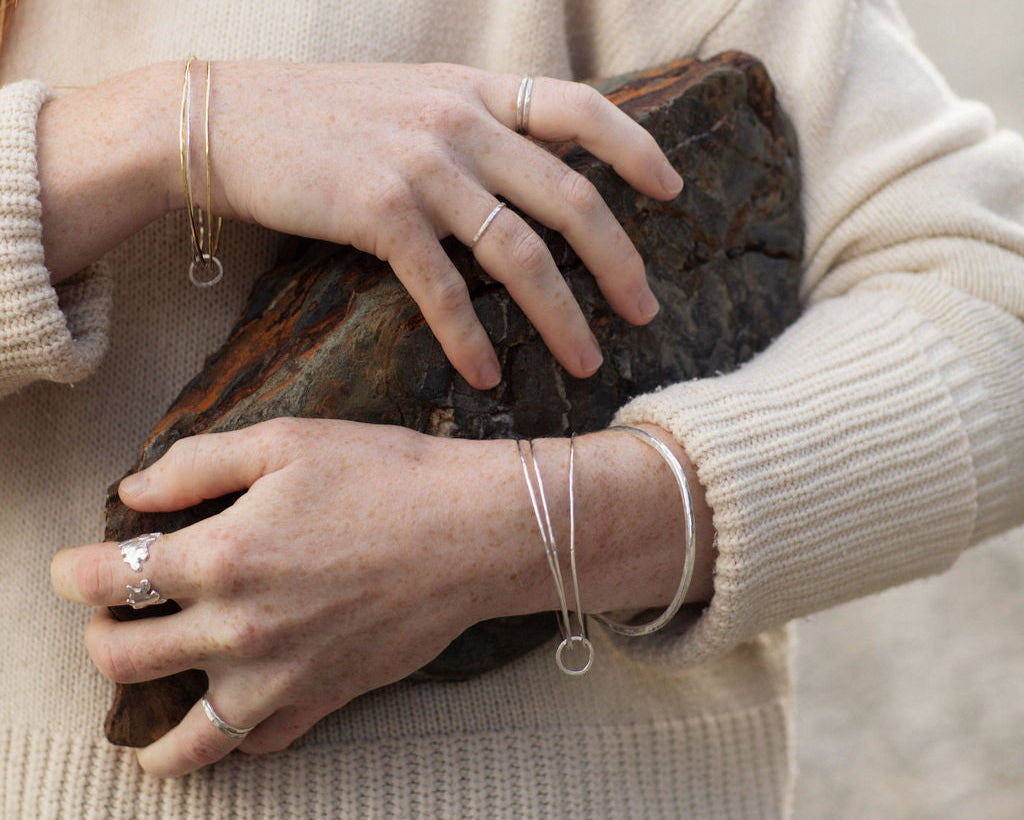 Person holding a rock with visible jewelry, wearing a beige sweater.