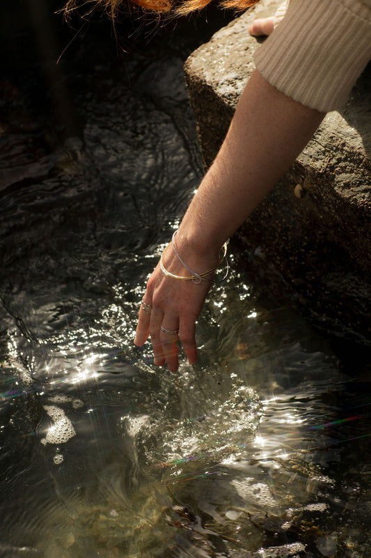 Hand reaching into a stream wearing bangles with a blurred background