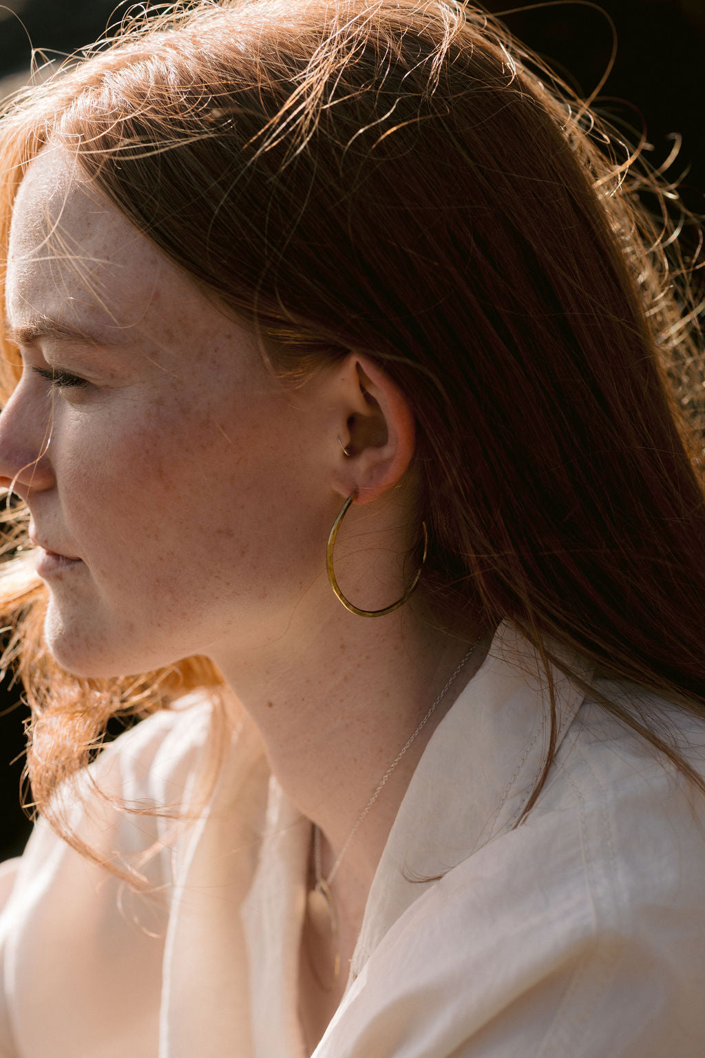 Lady with red hair and white shirt wearing brass hoops