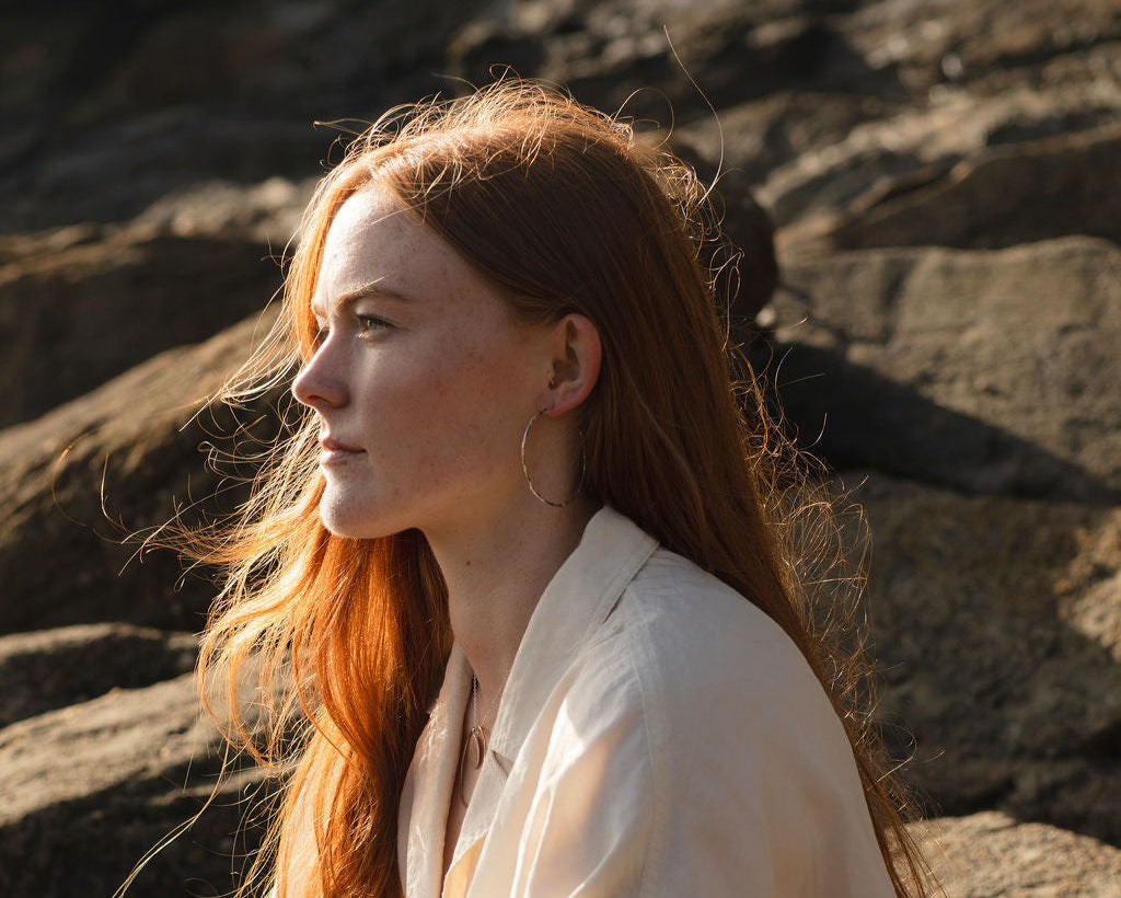 Woman with long red hair sitting against a rocky background