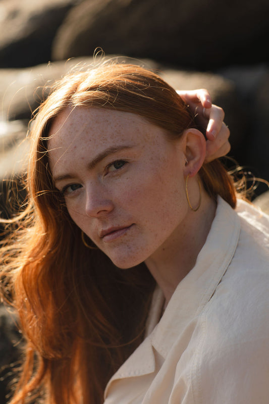 Woman with red hair and freckles adjusting her hair outdoors