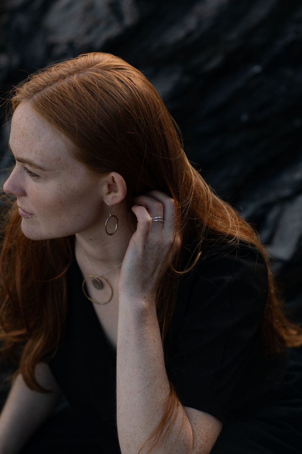 Woman with red hair wearing gold hoop earrings against a dark background