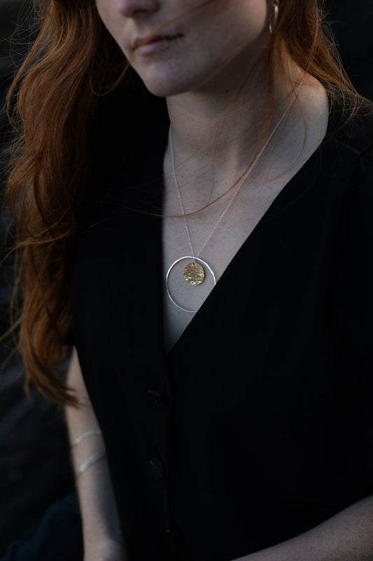 Person wearing a black top with a necklace featuring a circular pendant.