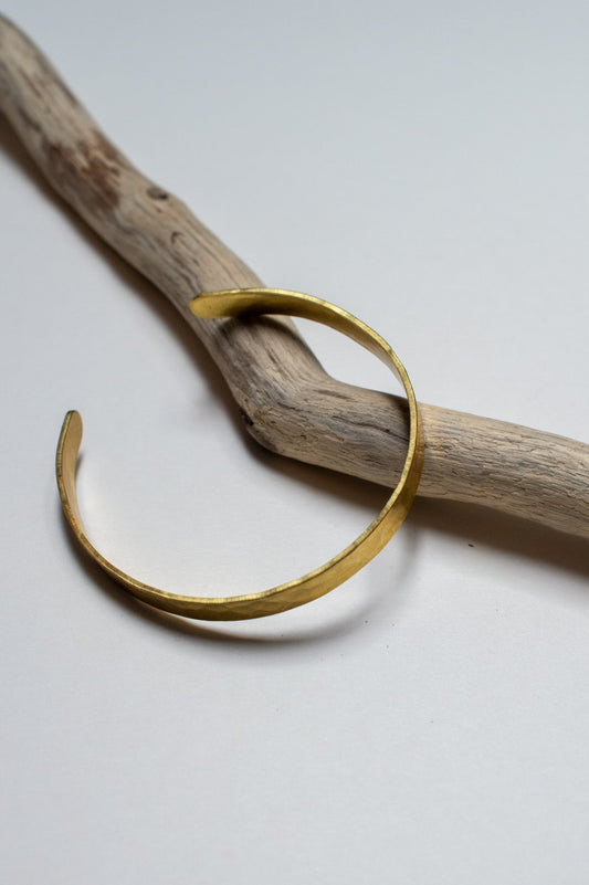 brass bracelet on a piece of driftwood against a white background