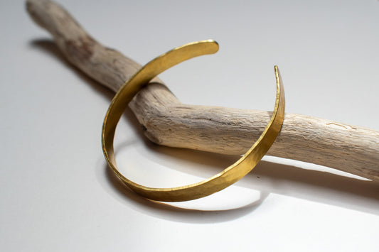brass bracelet on a piece of driftwood against a light background