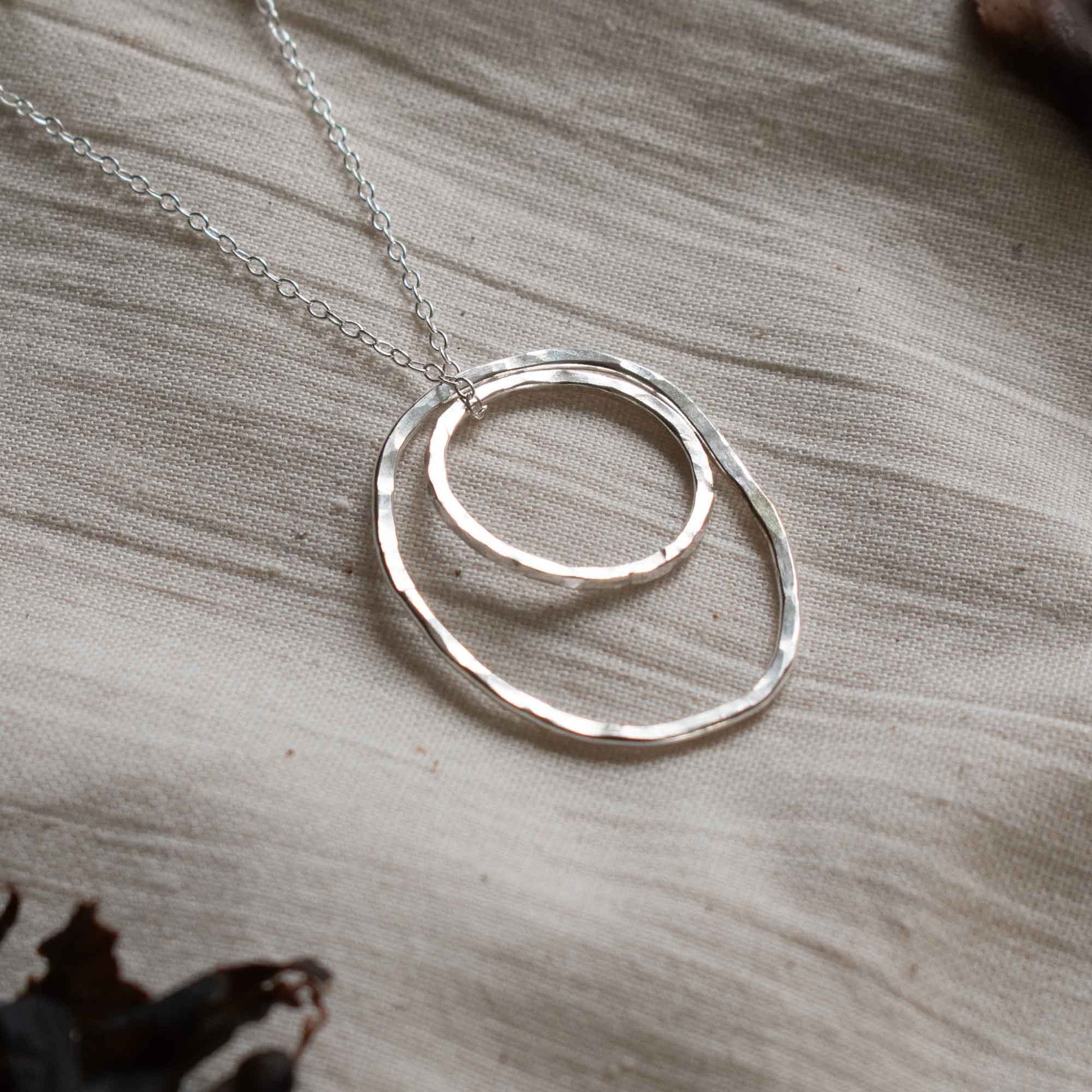Close up of a silver necklace made from two hammered silver hoops