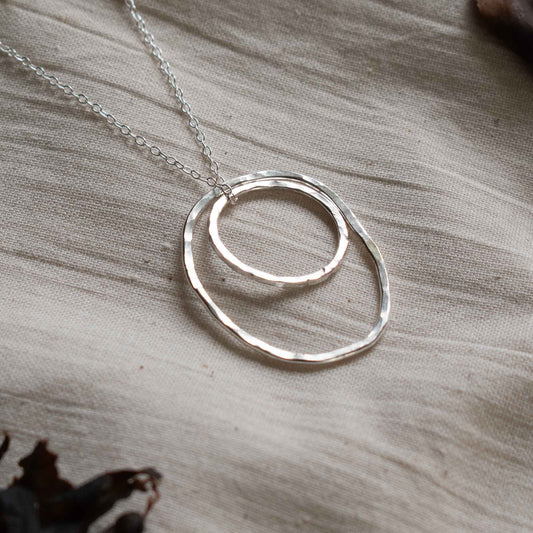 Close up of a silver necklace made from two hammered silver hoops