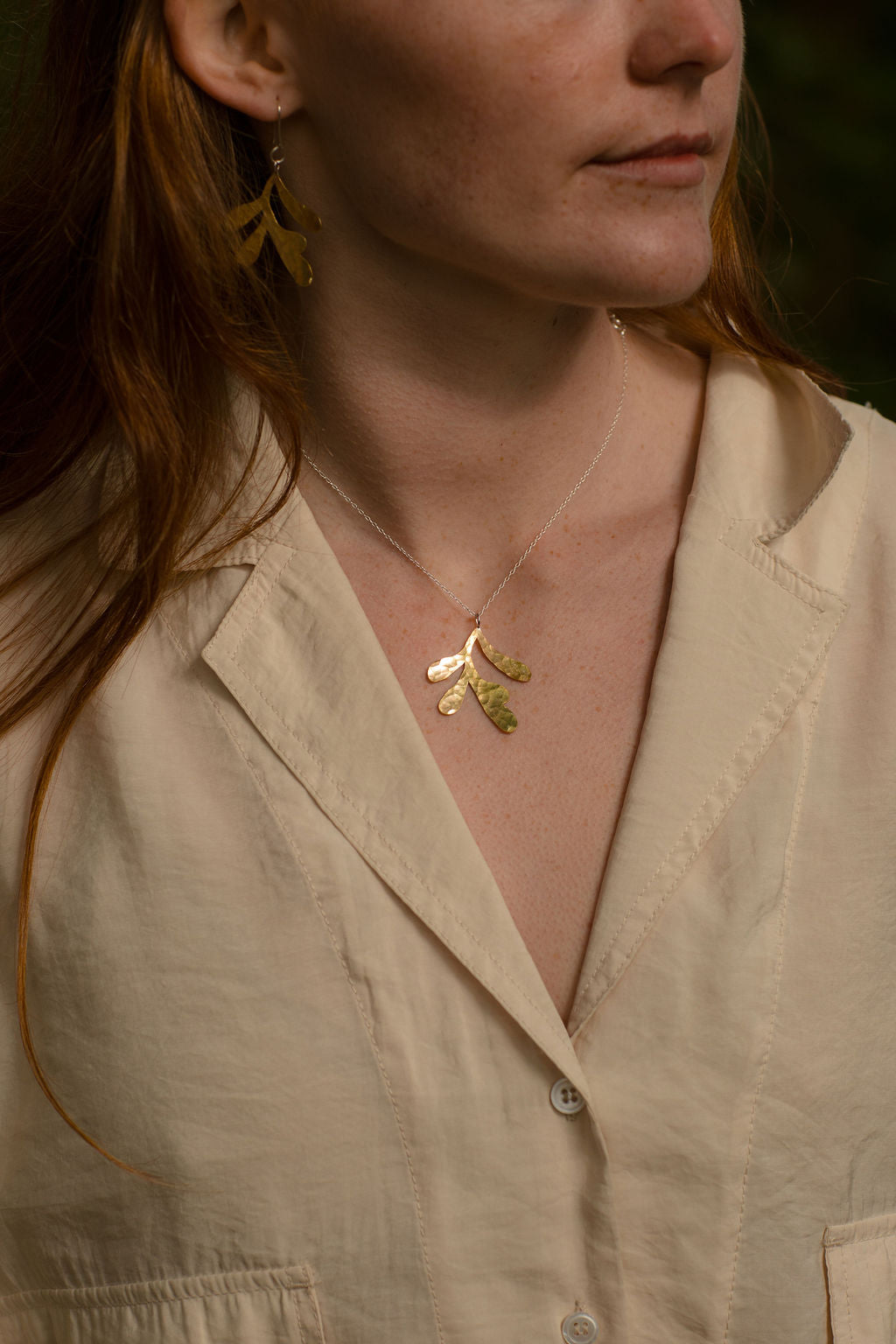 Woman wearing a silver necklace with a seaweed pendant against a neutral background